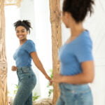 Woman Looks in Mirror Considering Tummy Tuck or Body Lift
