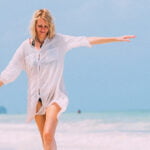 Mature Woman Raised Arms Walking Along the Beach
