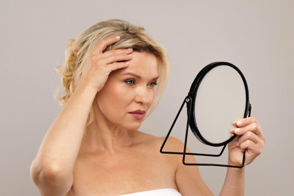 Mature woman looking at aging brow and forehead in the mirror